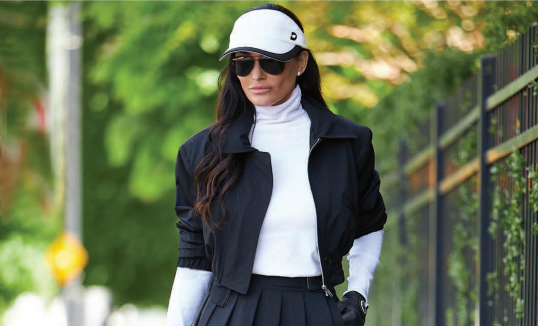 A woman wearing a hat and sunglasses is walking down the street.