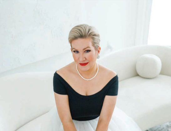 A woman in a black top and white skirt is sitting on a white couch