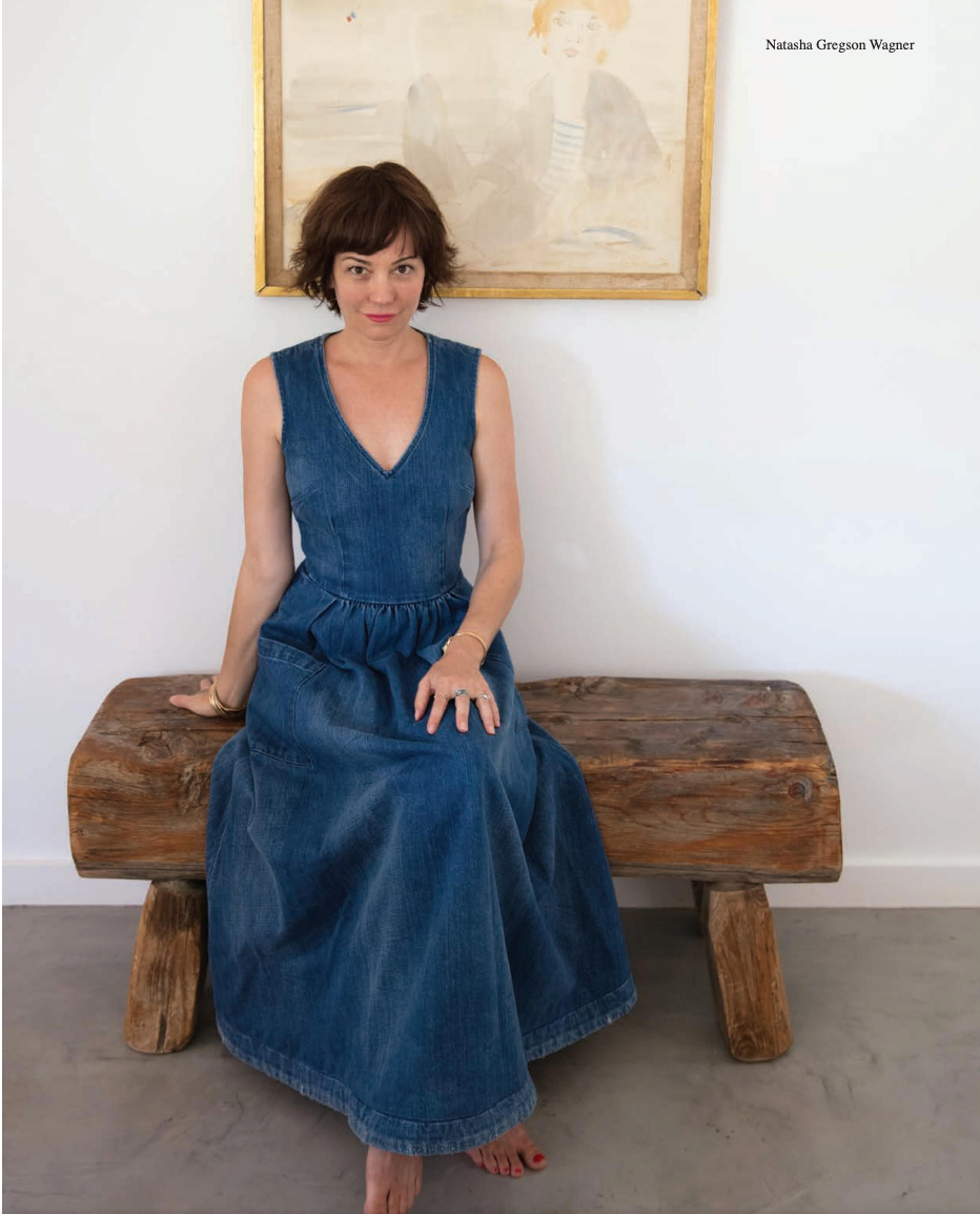 A woman in a denim dress is sitting on a wooden bench