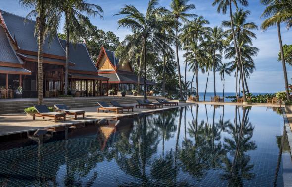 A large swimming pool surrounded by palm trees in front of a house.