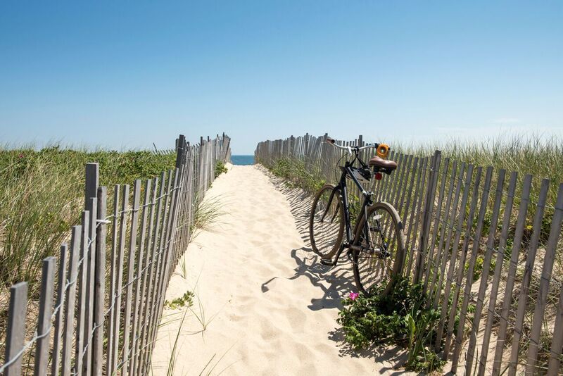 A bicycle is parked on the side of a sandy path leading to the beach.