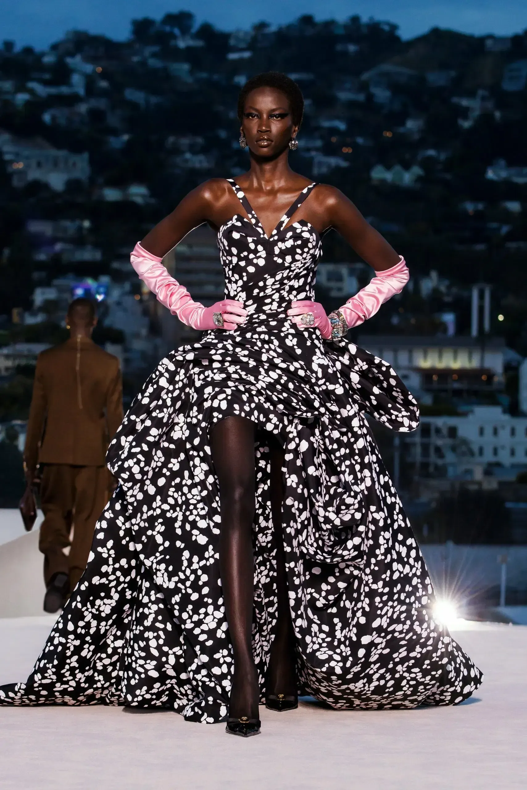 A model wearing a black and white dress and pink gloves