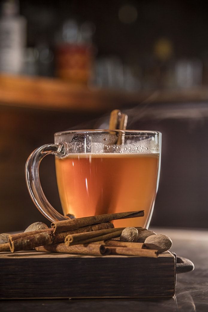 A cup of mulled wine with cinnamon sticks on a wooden cutting board.