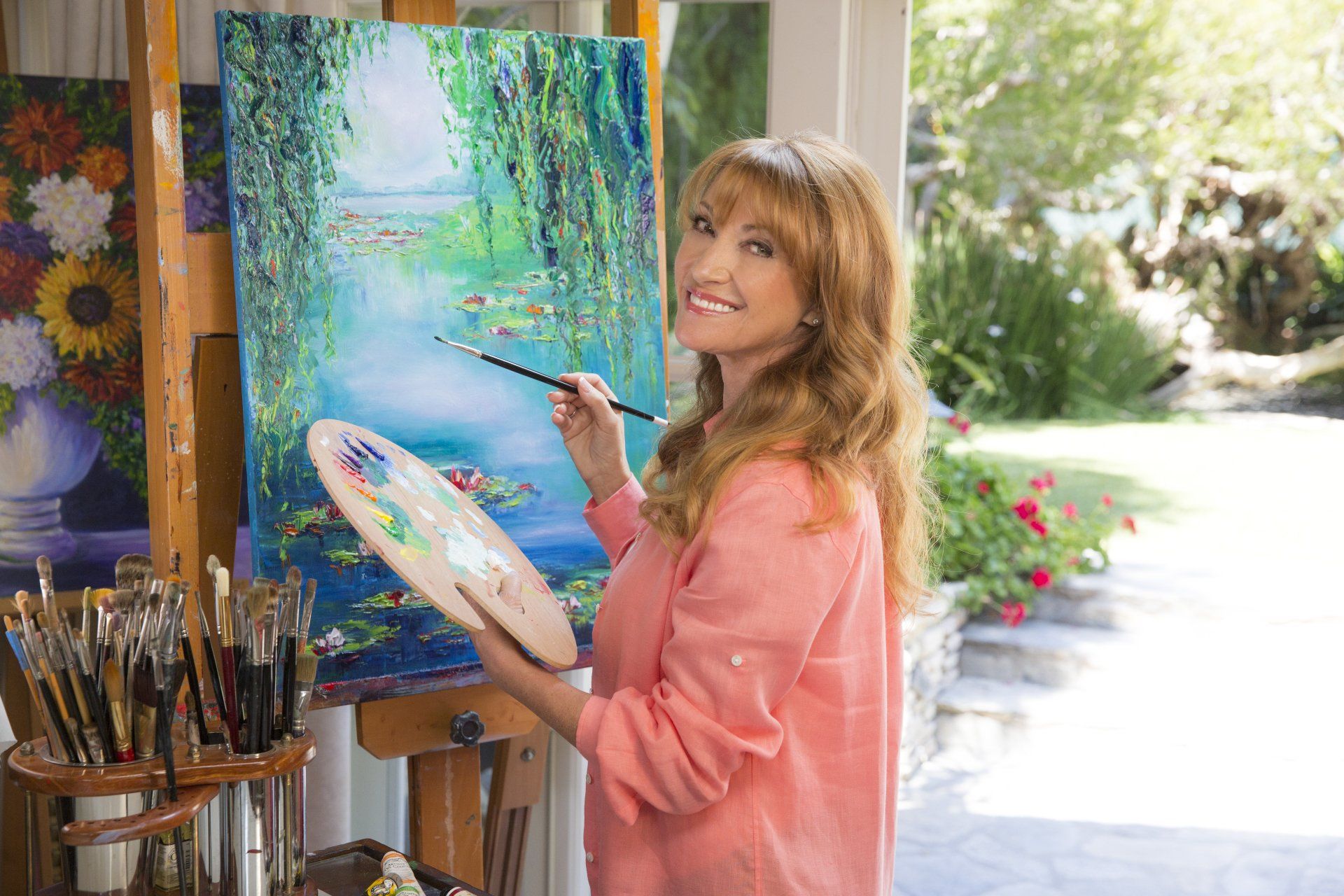 A woman is painting a picture on an easel with a brush and palette.