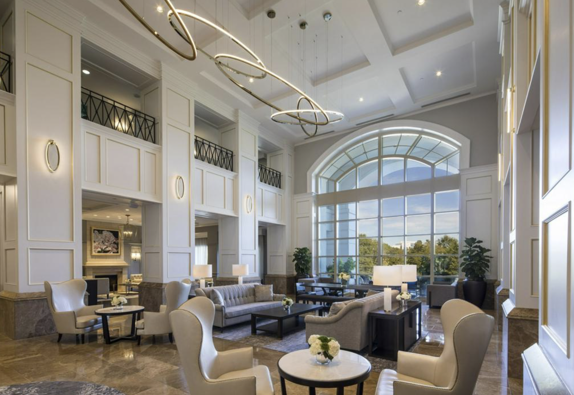 A large living room with a couch , chairs , tables and a chandelier.