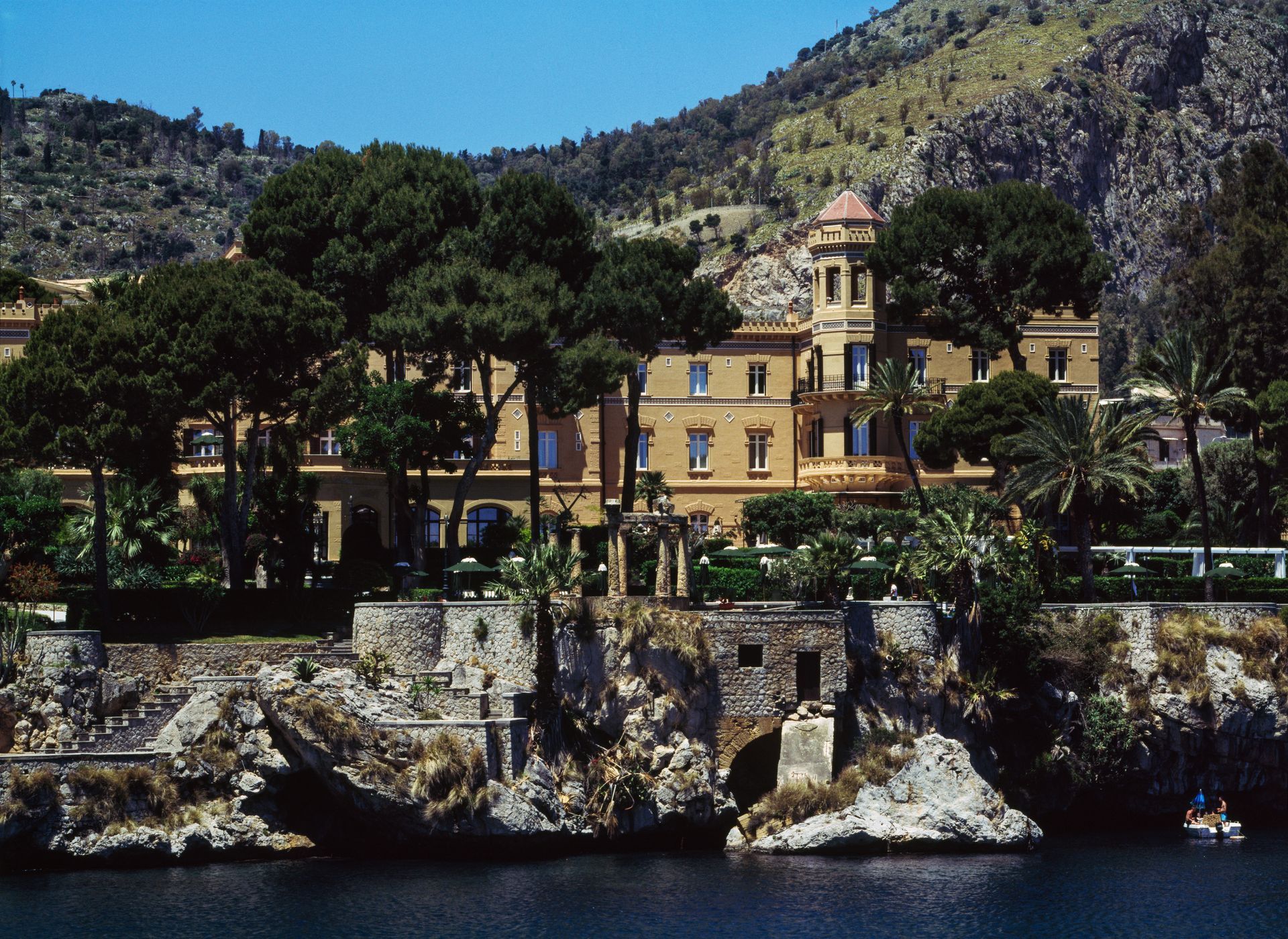 A large building sits on a cliff overlooking a body of water