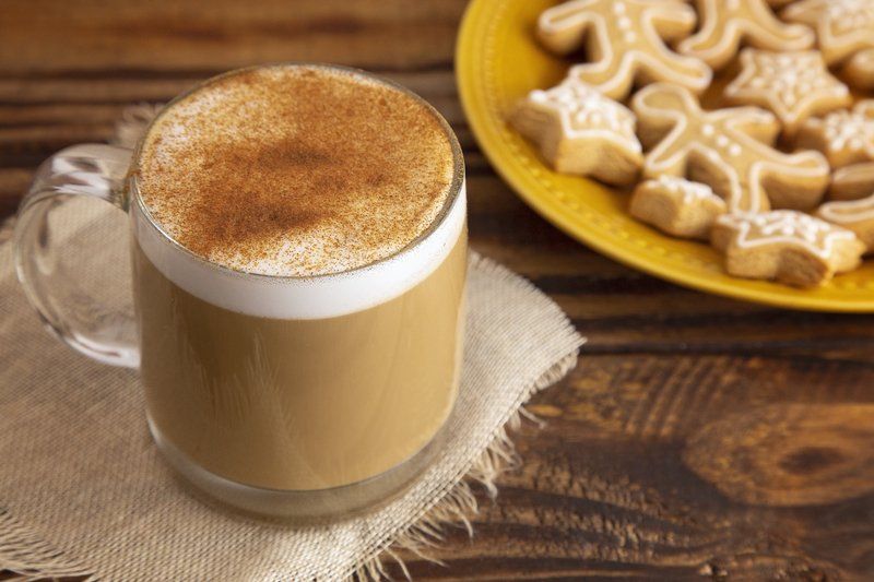 A cup of coffee and a plate of gingerbread cookies on a wooden table.