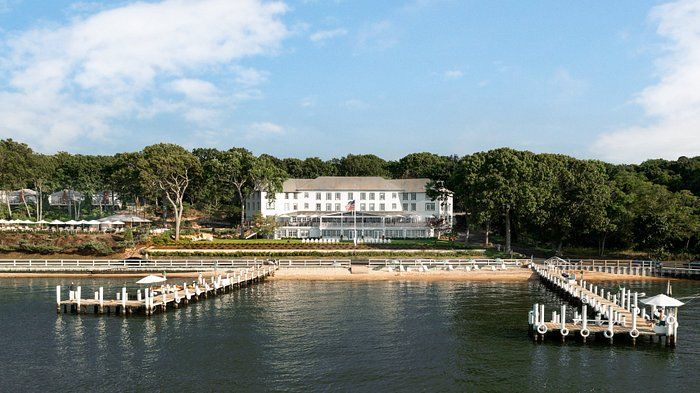 A large white house is sitting on top of a body of water surrounded by trees.