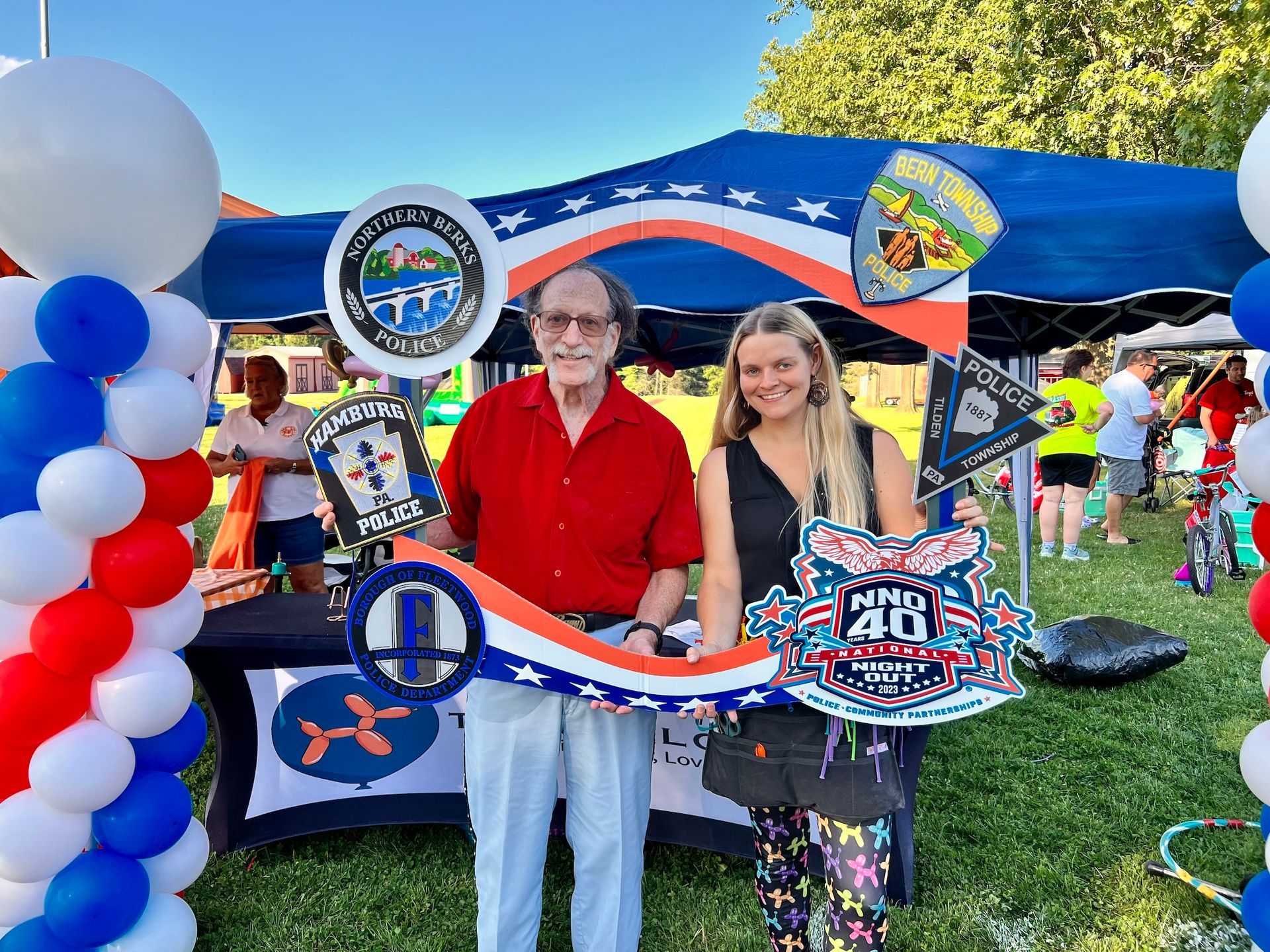 A man and a woman are standing in front of a tent with balloons.