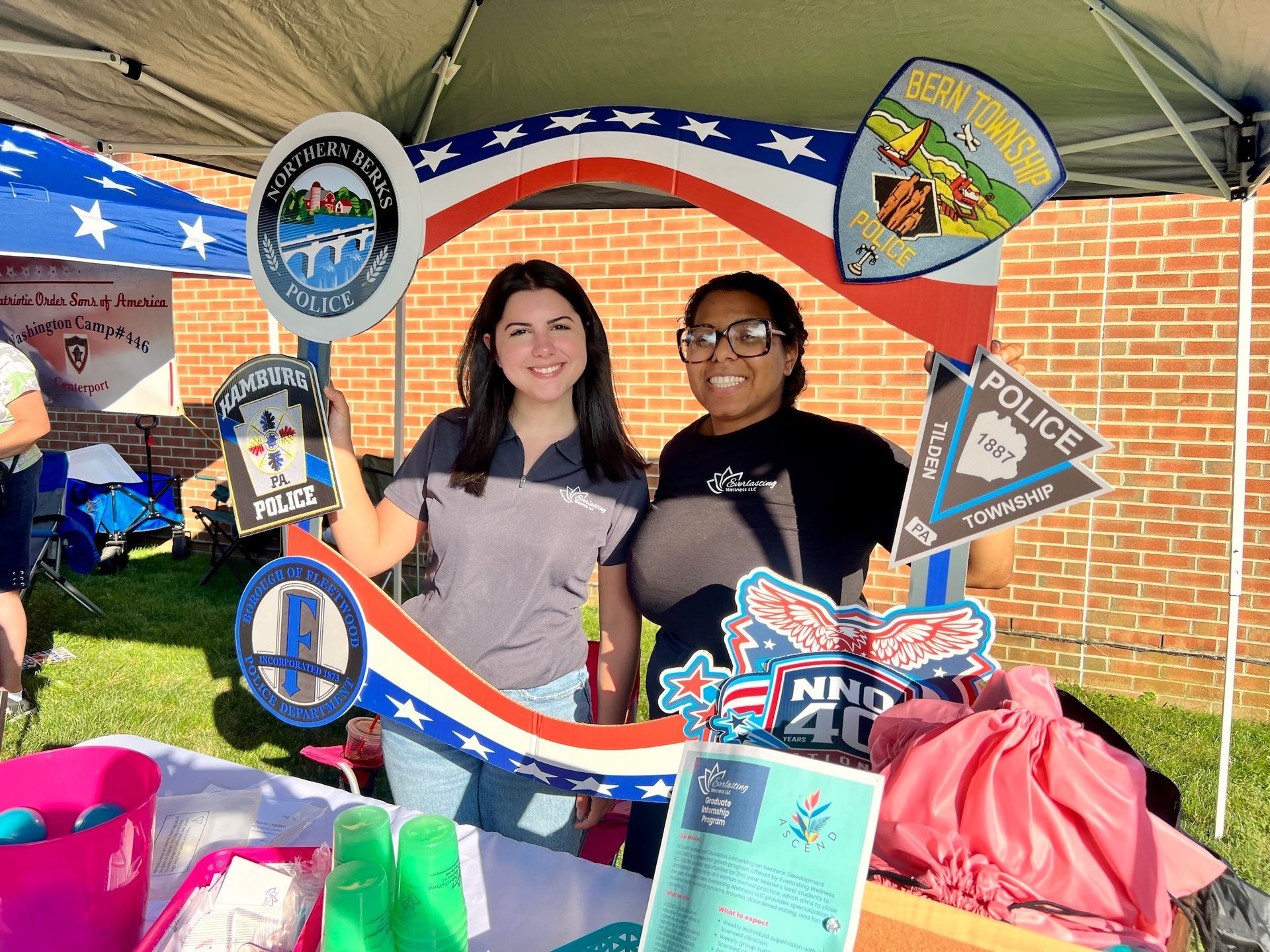 Two women are posing for a picture under a tent.