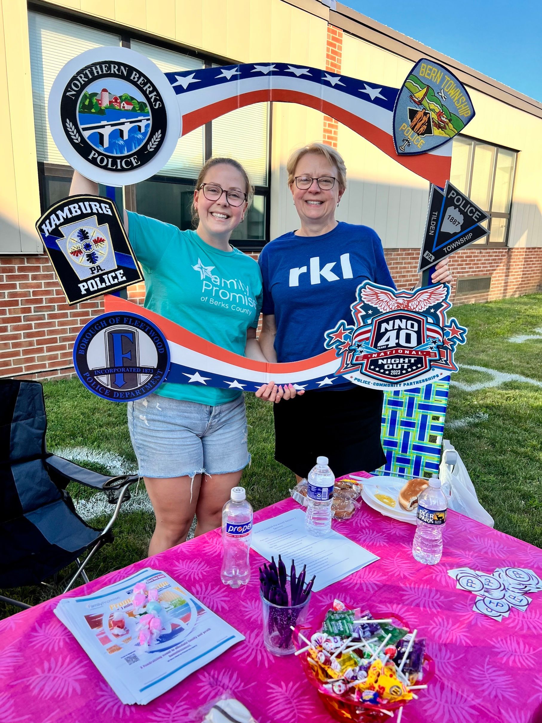 Two women are posing for a picture in front of a table.