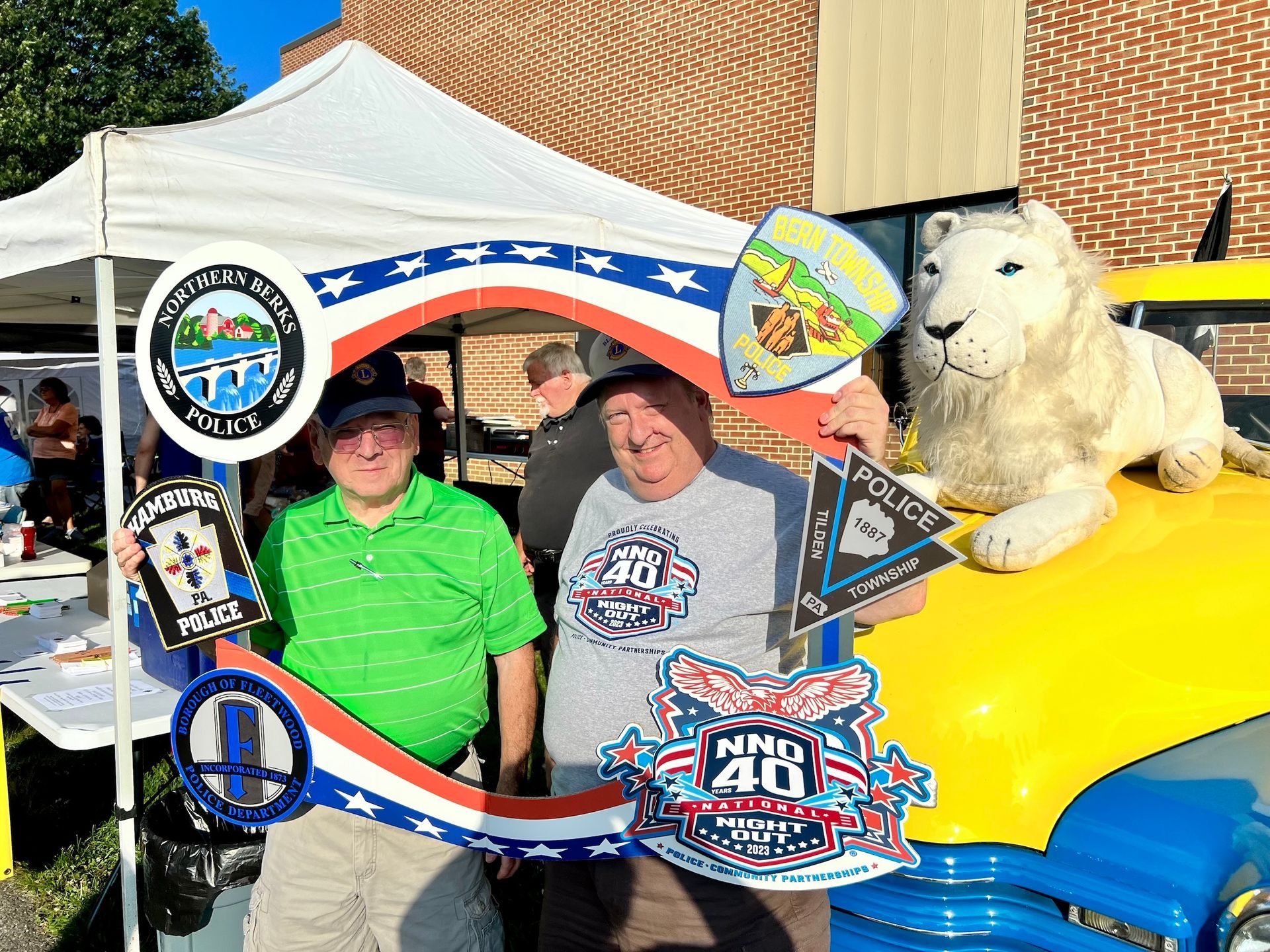 Two men are posing for a picture with a lion on top of a car.