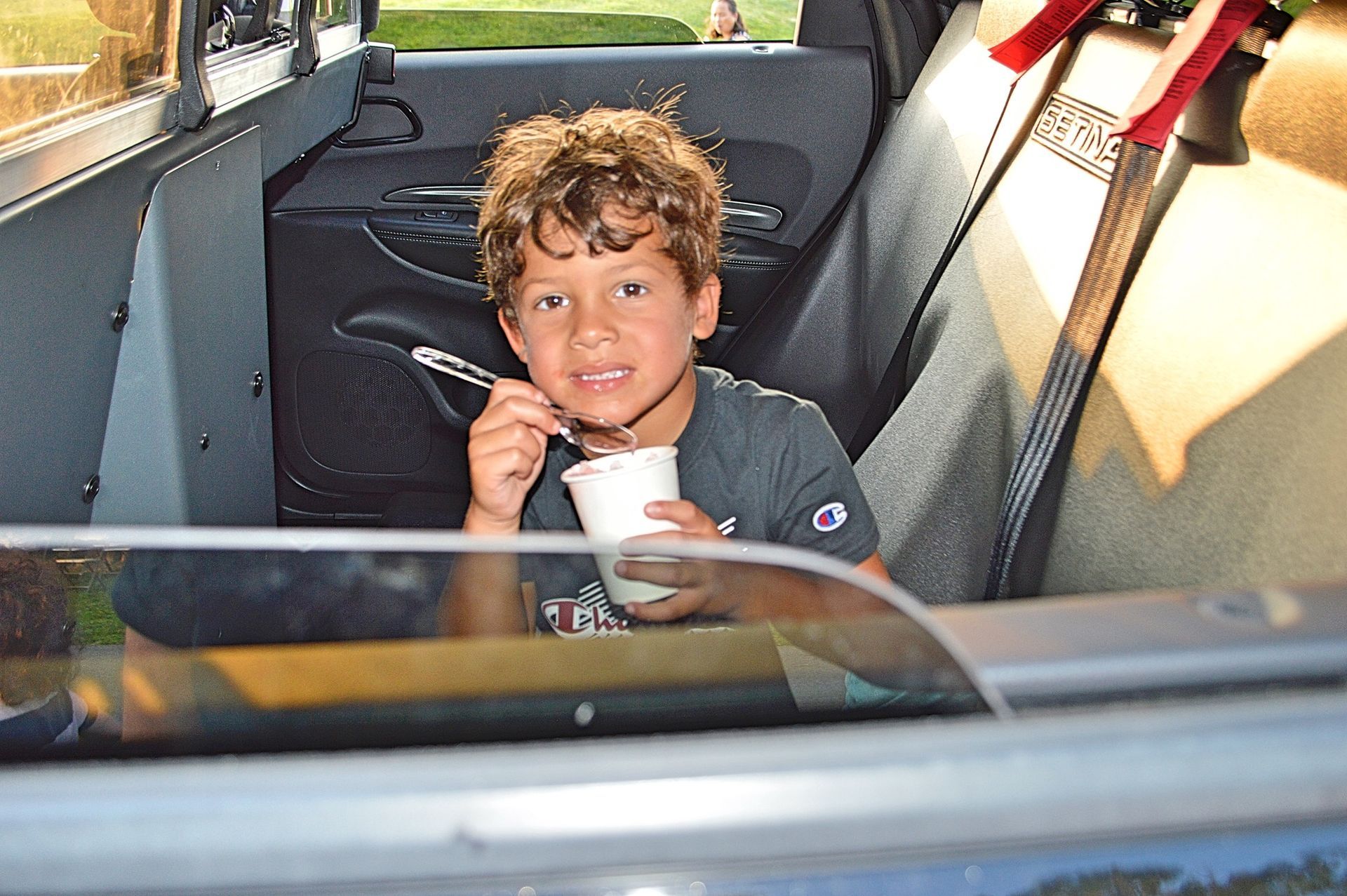 A young boy is eating ice cream in the back seat of a car