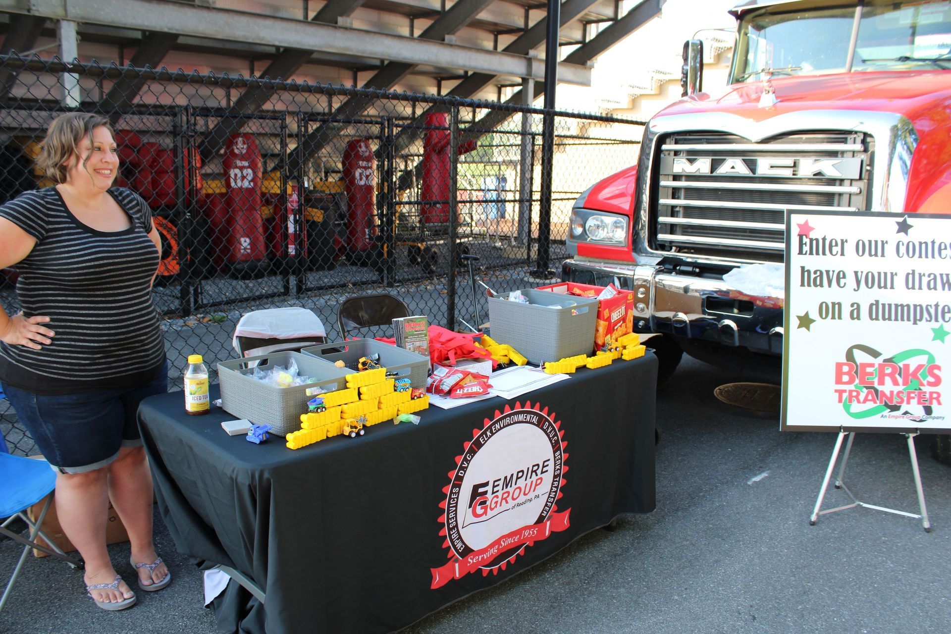 A woman stands in front of a table with a sign that says enter our contest have your draw on a dumpster