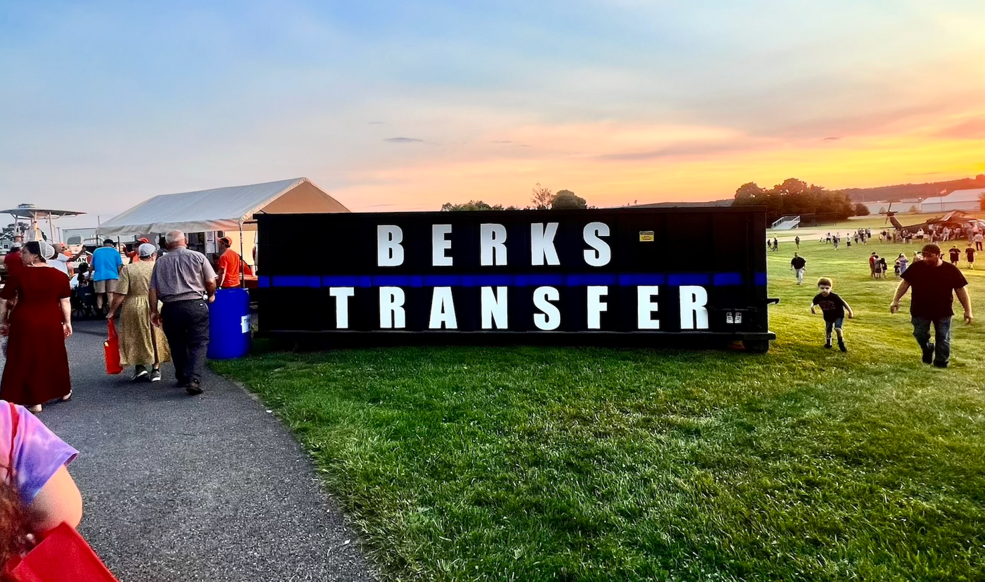 A group of people are walking in front of a large sign that says berks transfer.