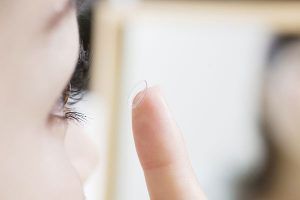 Person holding a contact lens near their eye in front of a mirror.