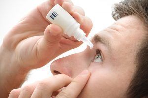 Person using eye drops, applying medication to their eye.