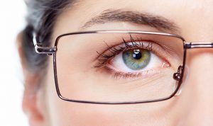 Close-up of a woman's eye, green iris, wearing square glasses.