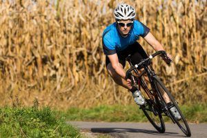 Cyclist in blue jersey and helmet leans into a turn on a road next to a field.