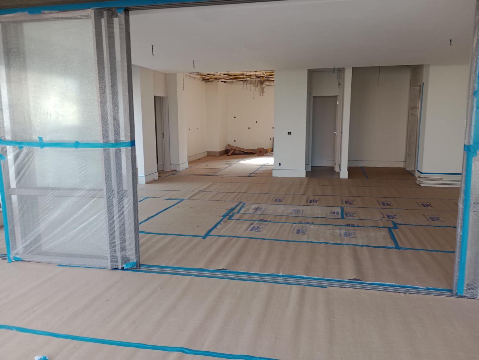 Quarto vazio em reforma, com lona plástica, proteção de piso com fita adesiva e portas expostas.