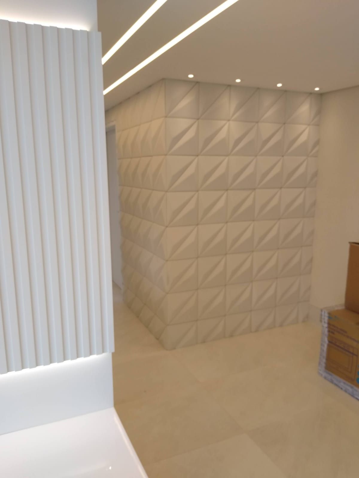 Interior moderno com painéis de parede 3D brancos, iluminação embutida e piso de azulejo bege.