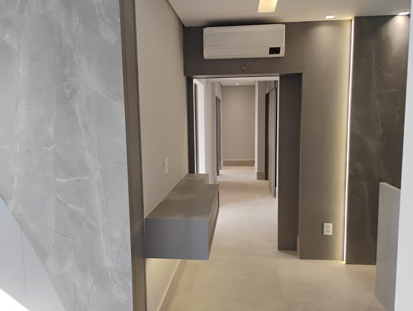 Interior de corredor moderno com paredes cinza, iluminação embutida e ar-condicionado de parede.