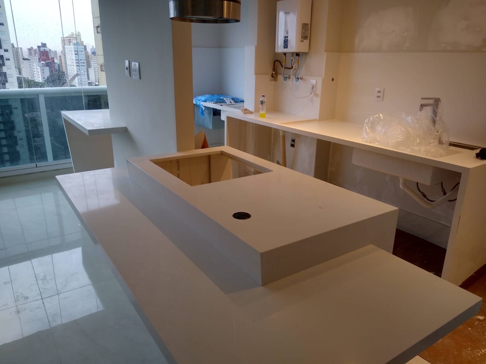 Cozinha moderna com ilha central branca, nicho para pia, armários bege e vista para a varanda.