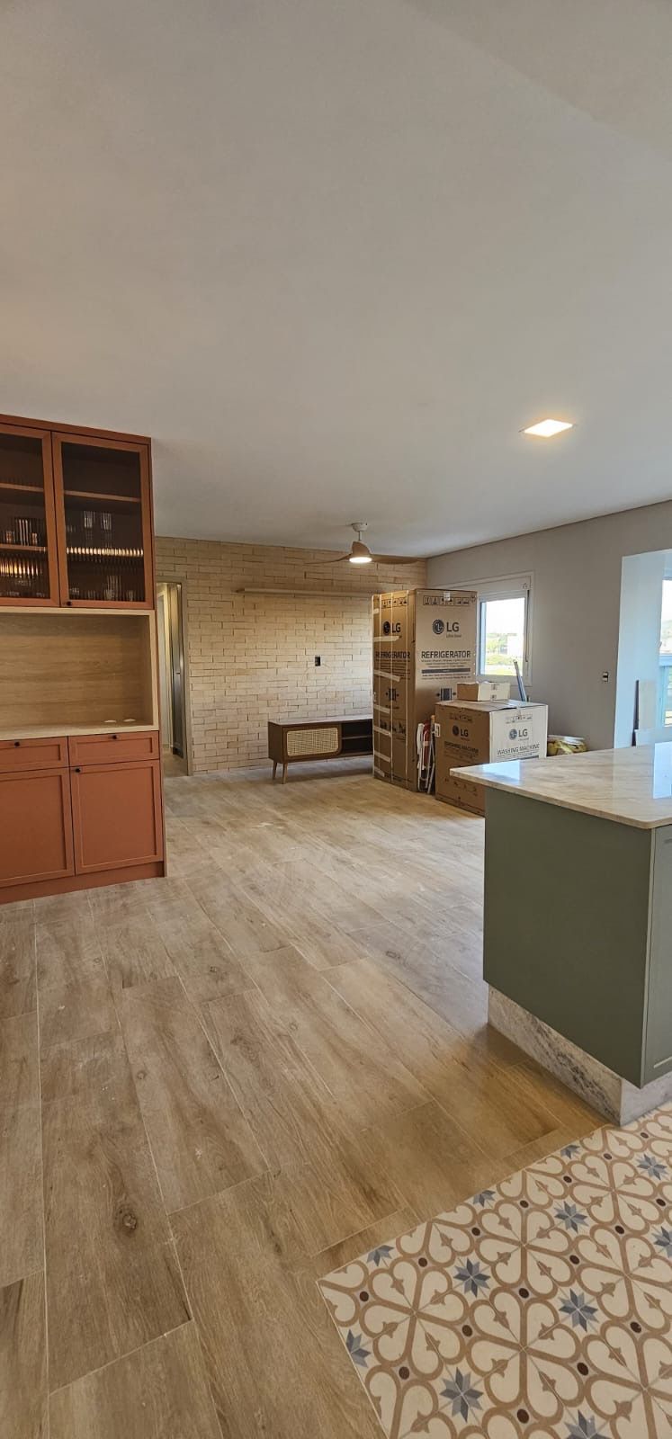 Cozinha e sala de estar integradas, com piso de madeira, armários brancos e uma pequena área revestida com azulejos.