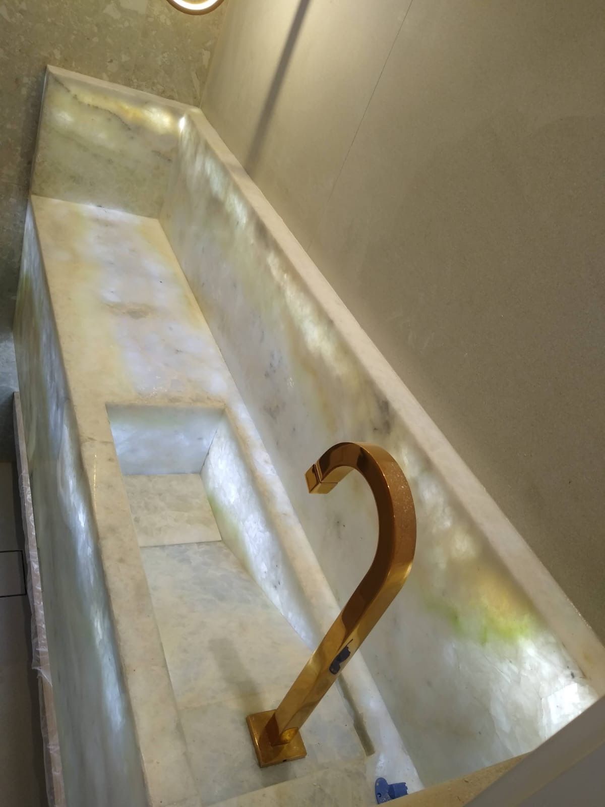 Gancho de metal enferrujado em uma bacia ou recipiente semelhante a uma banheira, revestido com azulejos brancos, contra uma parede bege.