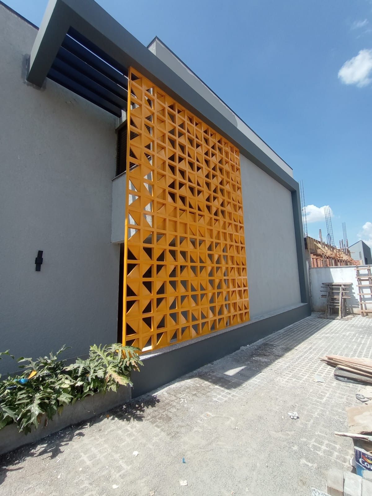 Prédio moderno cinza com um painel decorativo laranja vibrante na parede e calçada pavimentada sob um céu azul.
