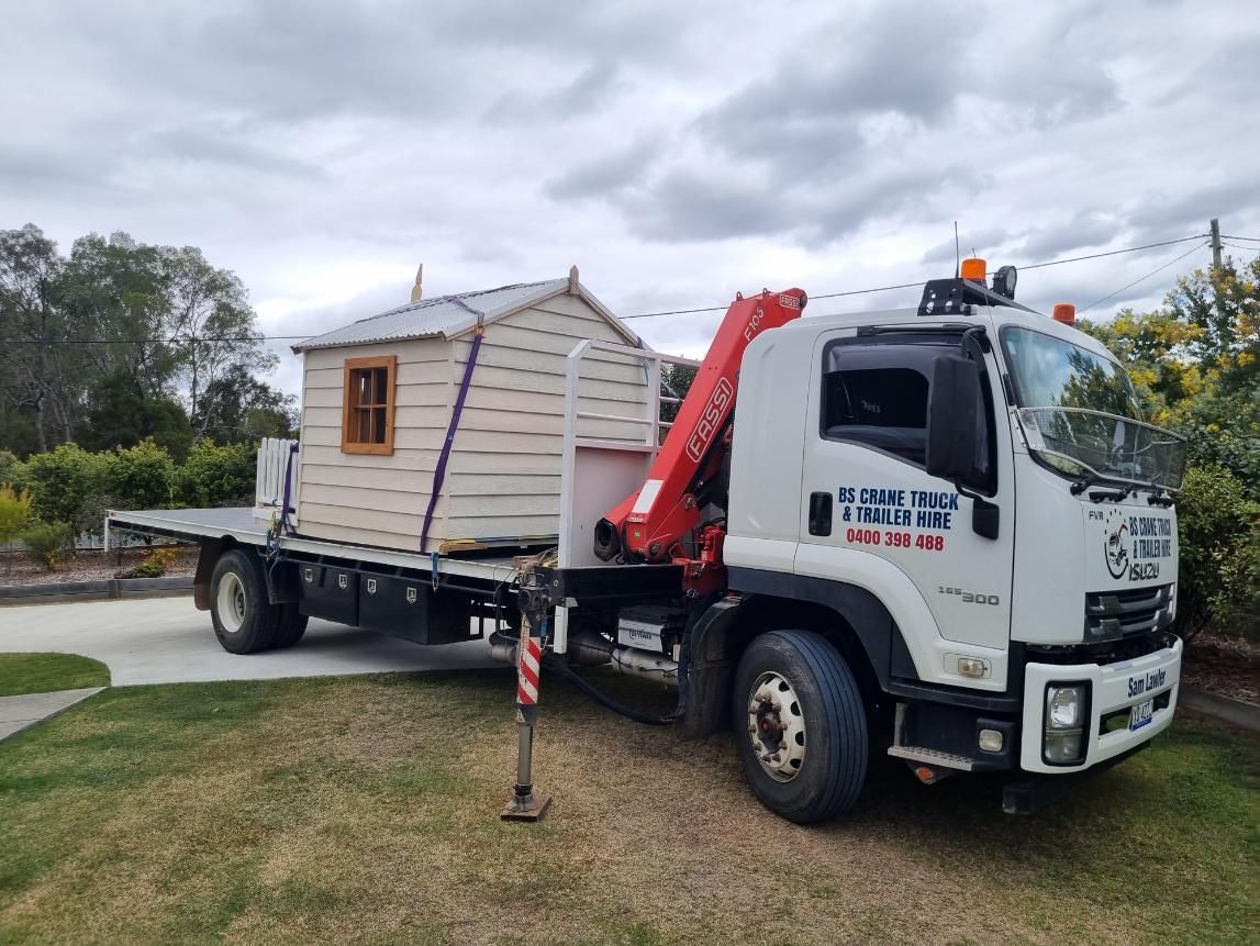 A Tow Truck is Carrying a Small Wooden House on a Trailer — BS Crane Truck and Trailer Hire In Cooroy, QLD