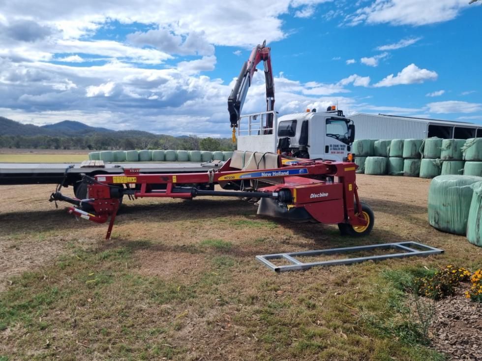 A Red Truck With a Crane Attached to It is Parked in a Field Next to Bales of Hay — BS Crane Truck and Trailer Hire In Yandina, QLD