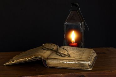 Open, ancient book in candlelight with glasses placed on top