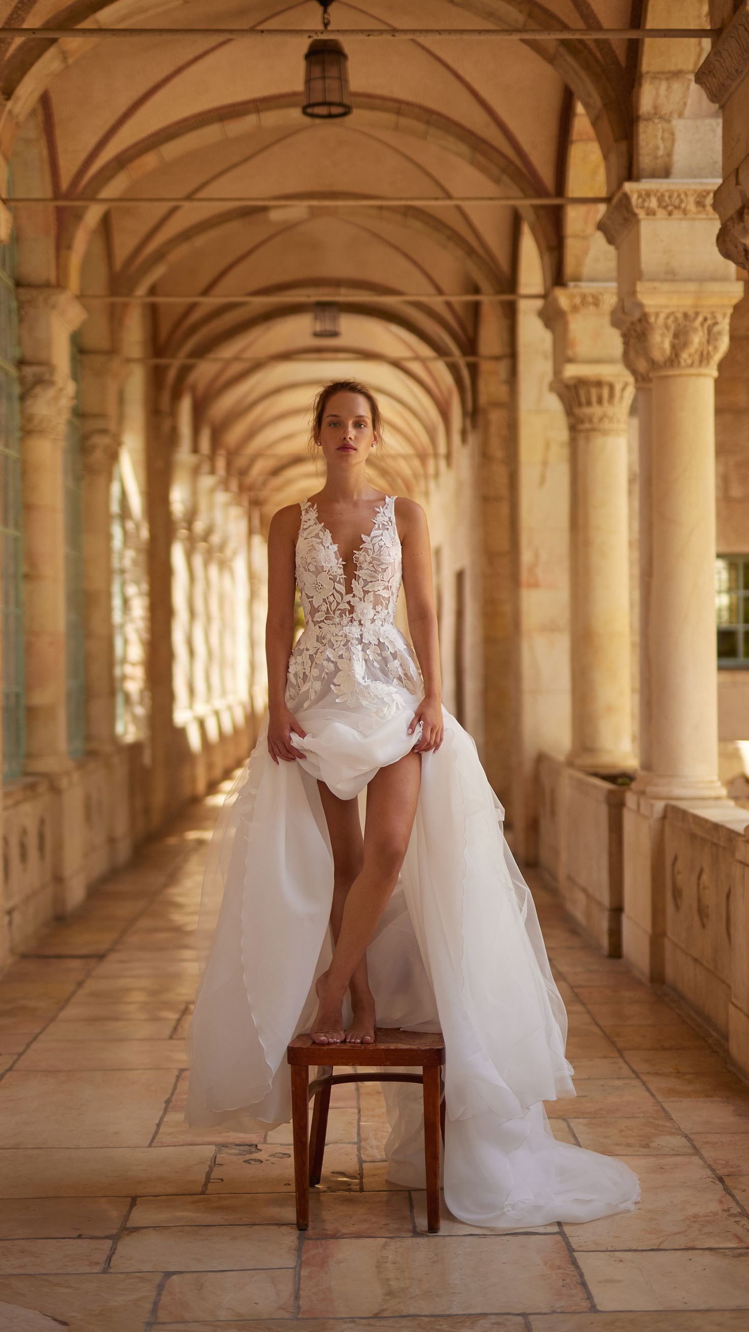 A woman in a wedding dress is sitting on a chair in a hallway.