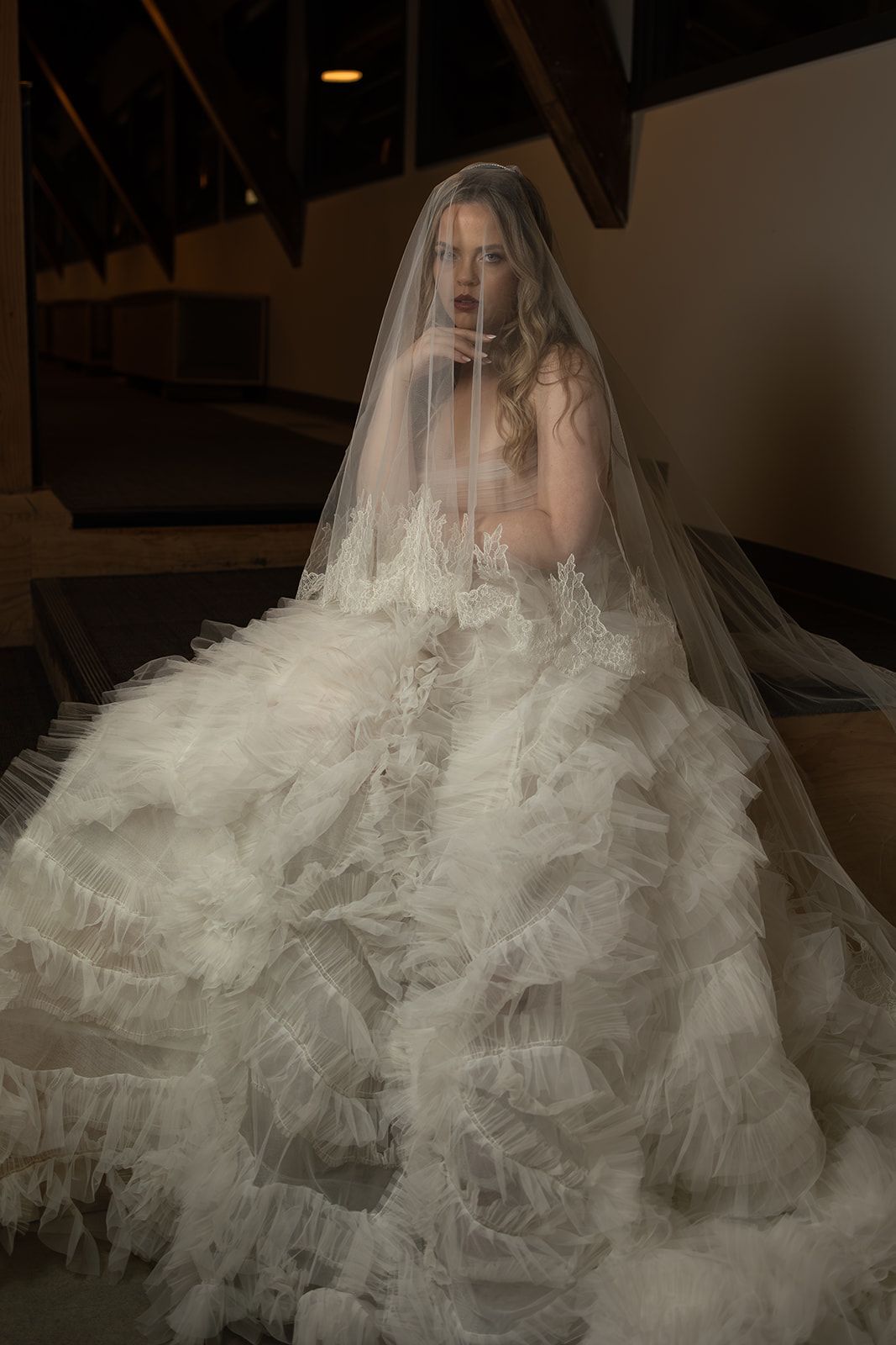 A bride with a unique bridal gown and veil posing in front of a white background