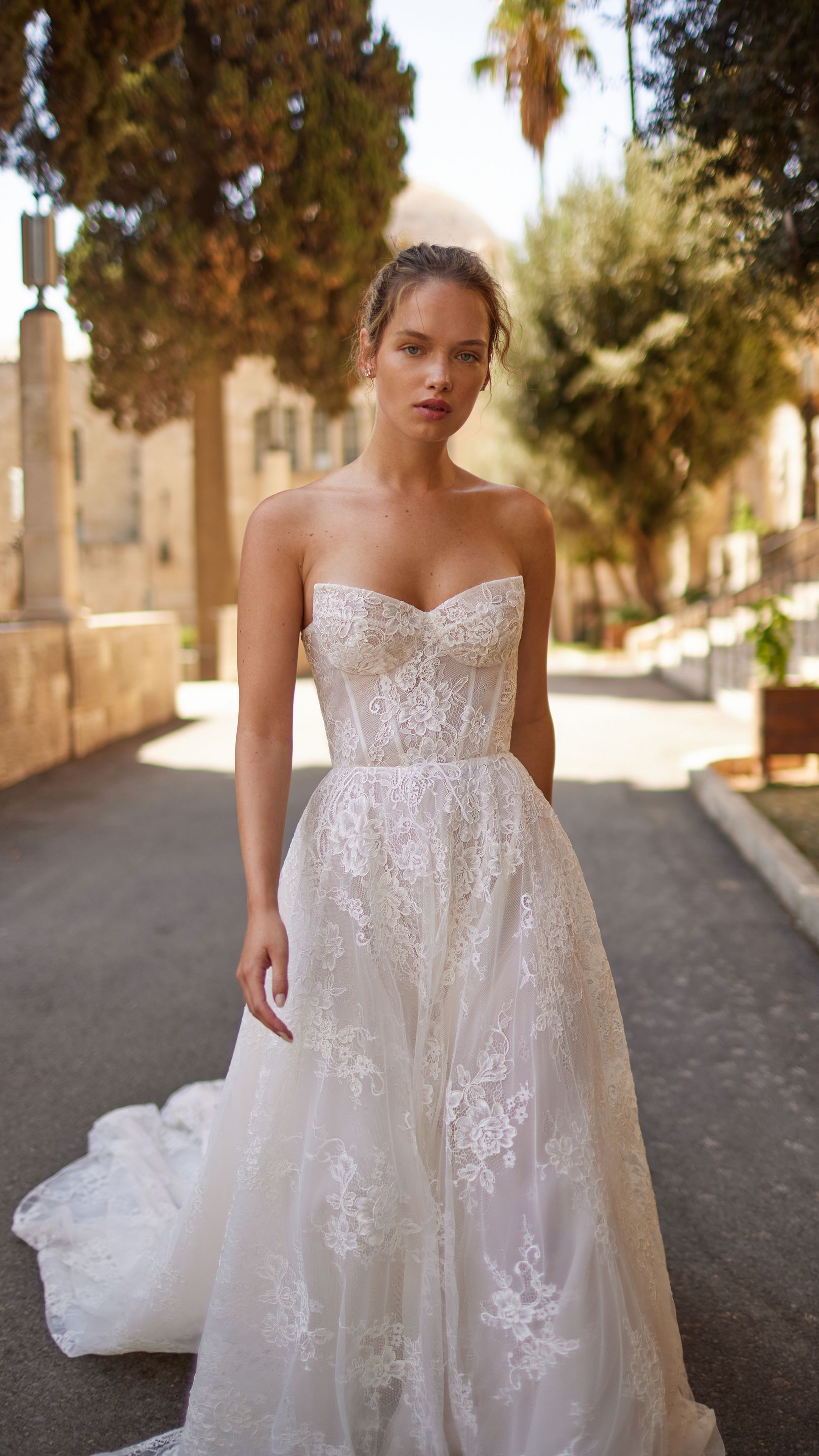 A woman in a white wedding dress is standing on a street.