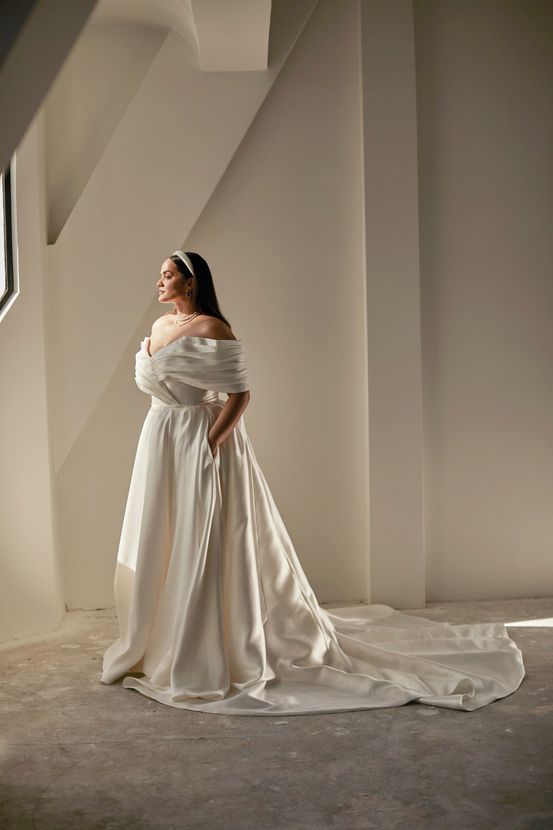 A woman in a white wedding dress is standing in front of a stone building.