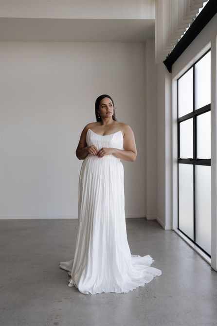 A woman in a wedding dress is standing next to a window.