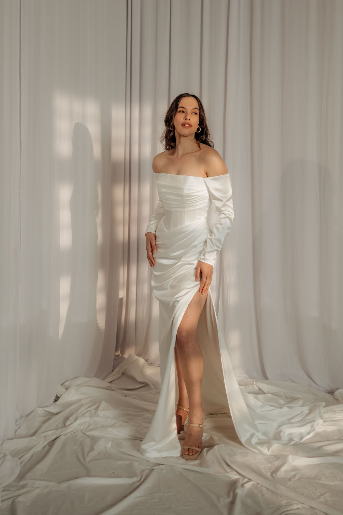 Elegant modern off-the-shoulders wedding gown with draping fabric and a leg slit