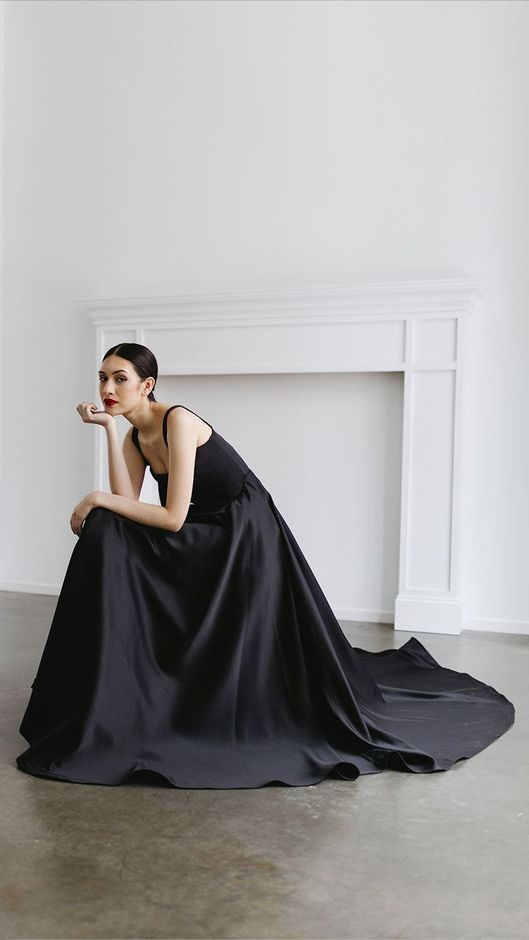 A woman in a black dress is sitting in front of a fireplace.