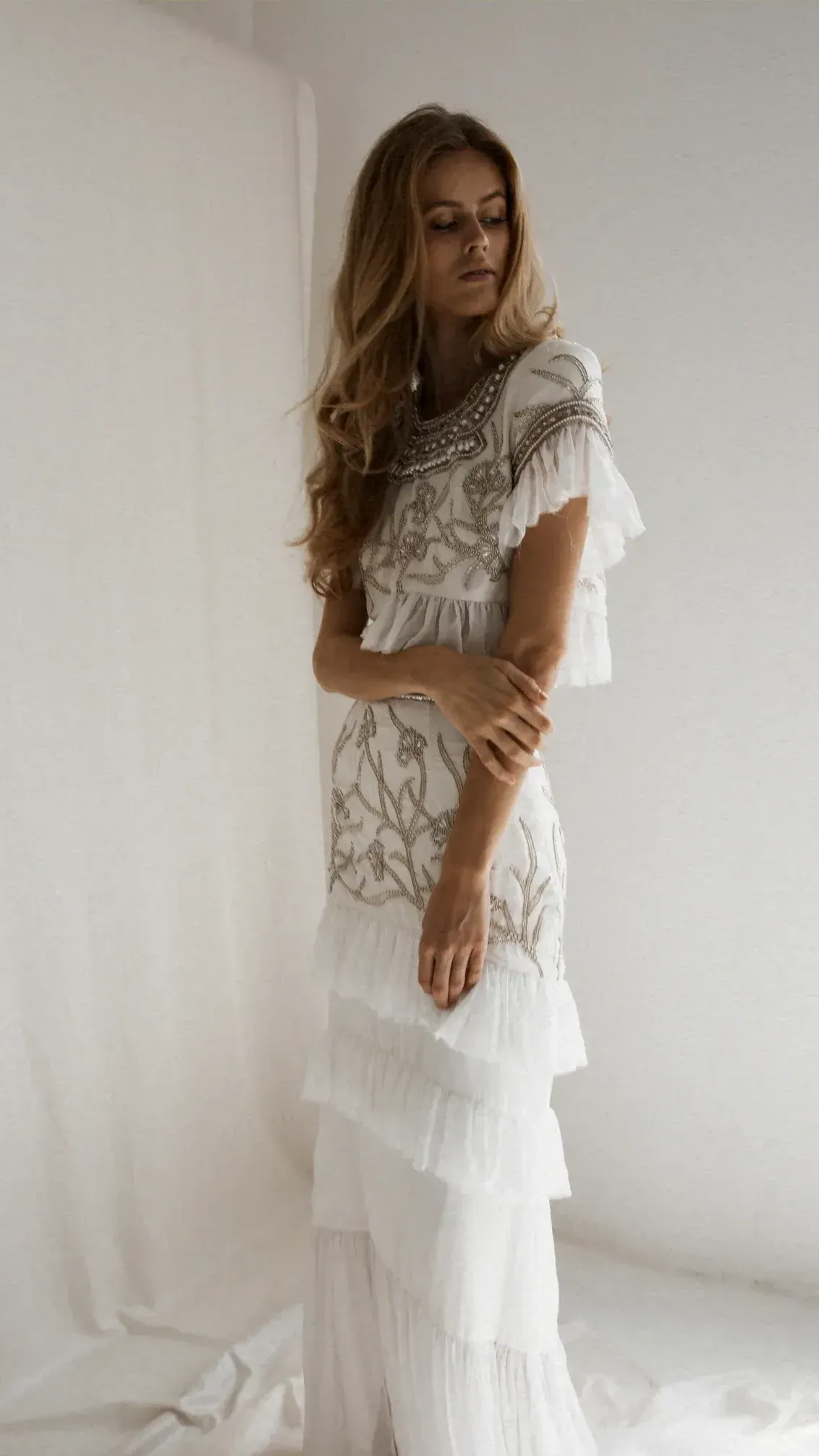 A woman in a white dress is standing in front of a white wall.