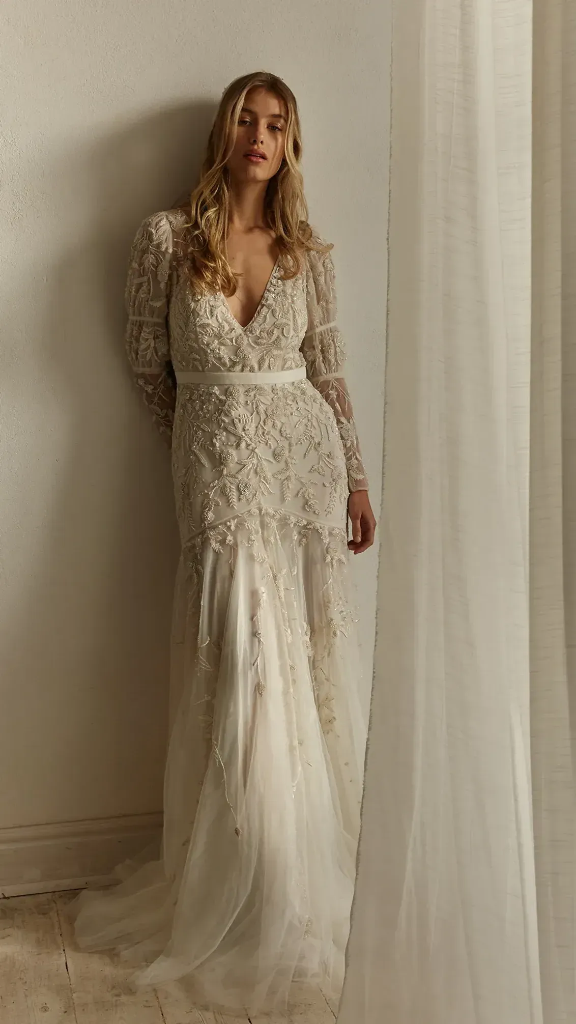 A woman in a white wedding dress is standing next to a window.