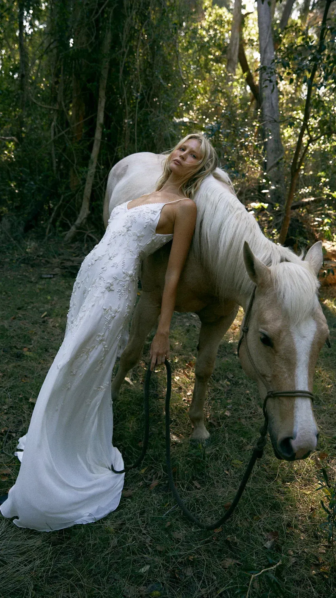 A woman in a wedding dress is standing next to a white horse.