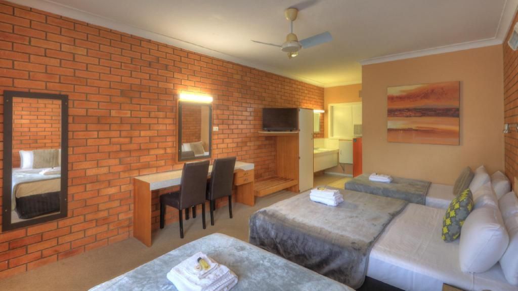 A Hotel Room With Three Beds, A Desk And A Mirror — Hilldrop Motor Inn In Waterview Heights, NSW