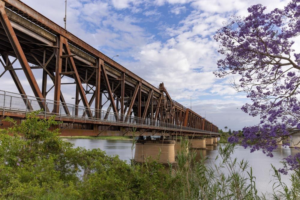 A Bridge Over A River With Purple Flowers — Hilldrop Motor Inn In Waterview Heights, NSW