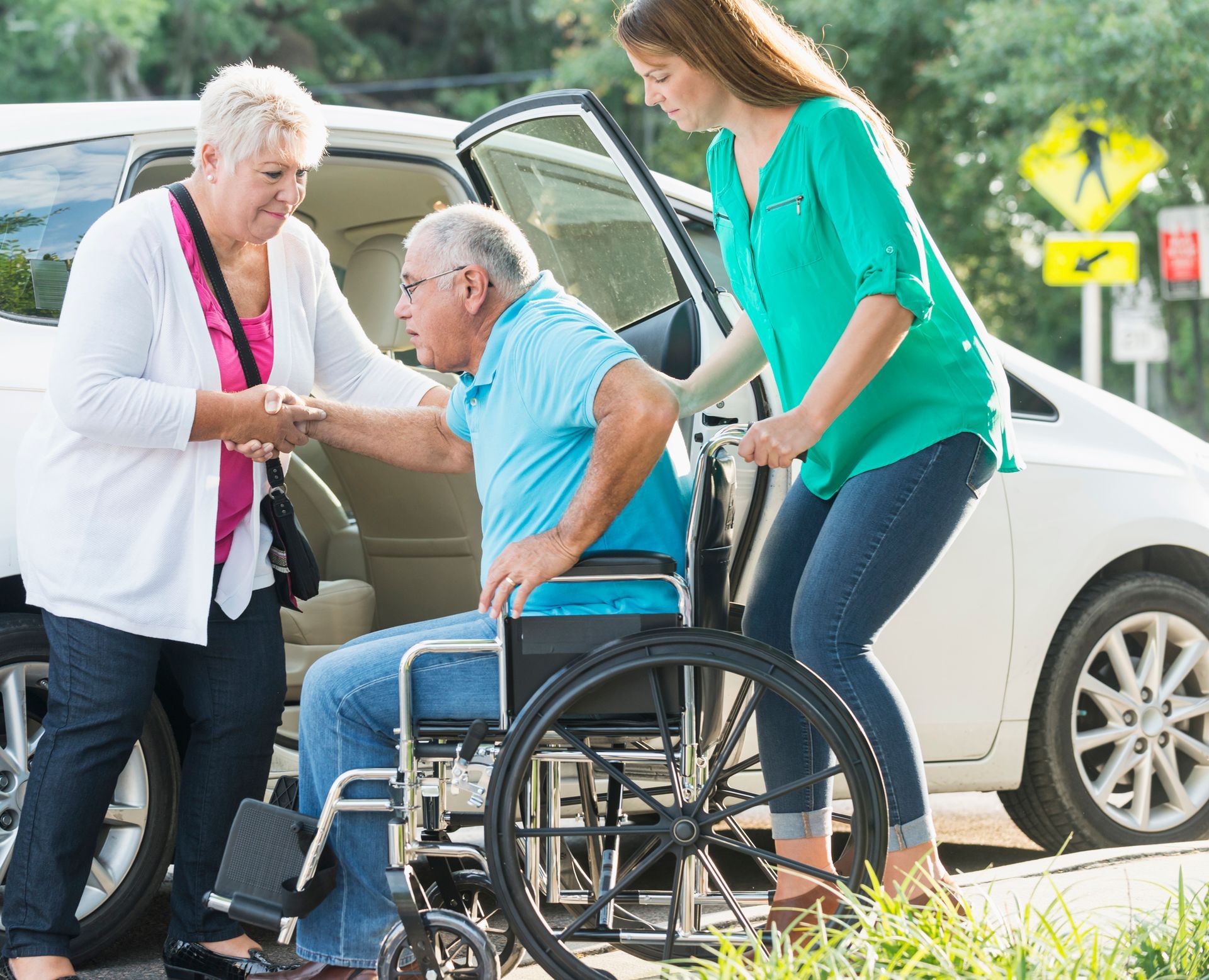 A woman is helping an elderly man in a wheelchair into a car.