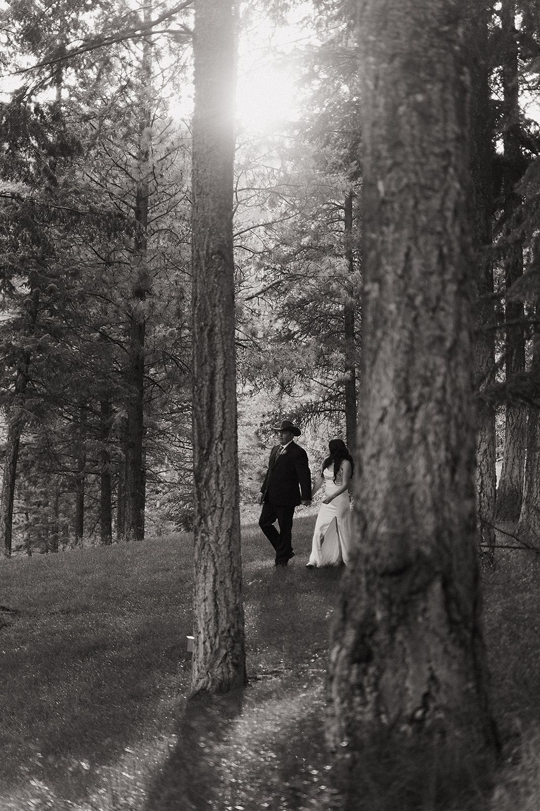A bride and groom are walking through a forest.