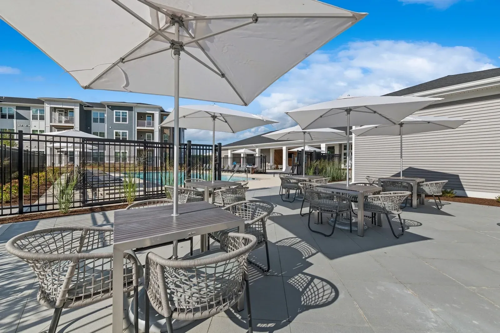 Outdoor community pool area with tables, chairs, and large white umbrellas.
