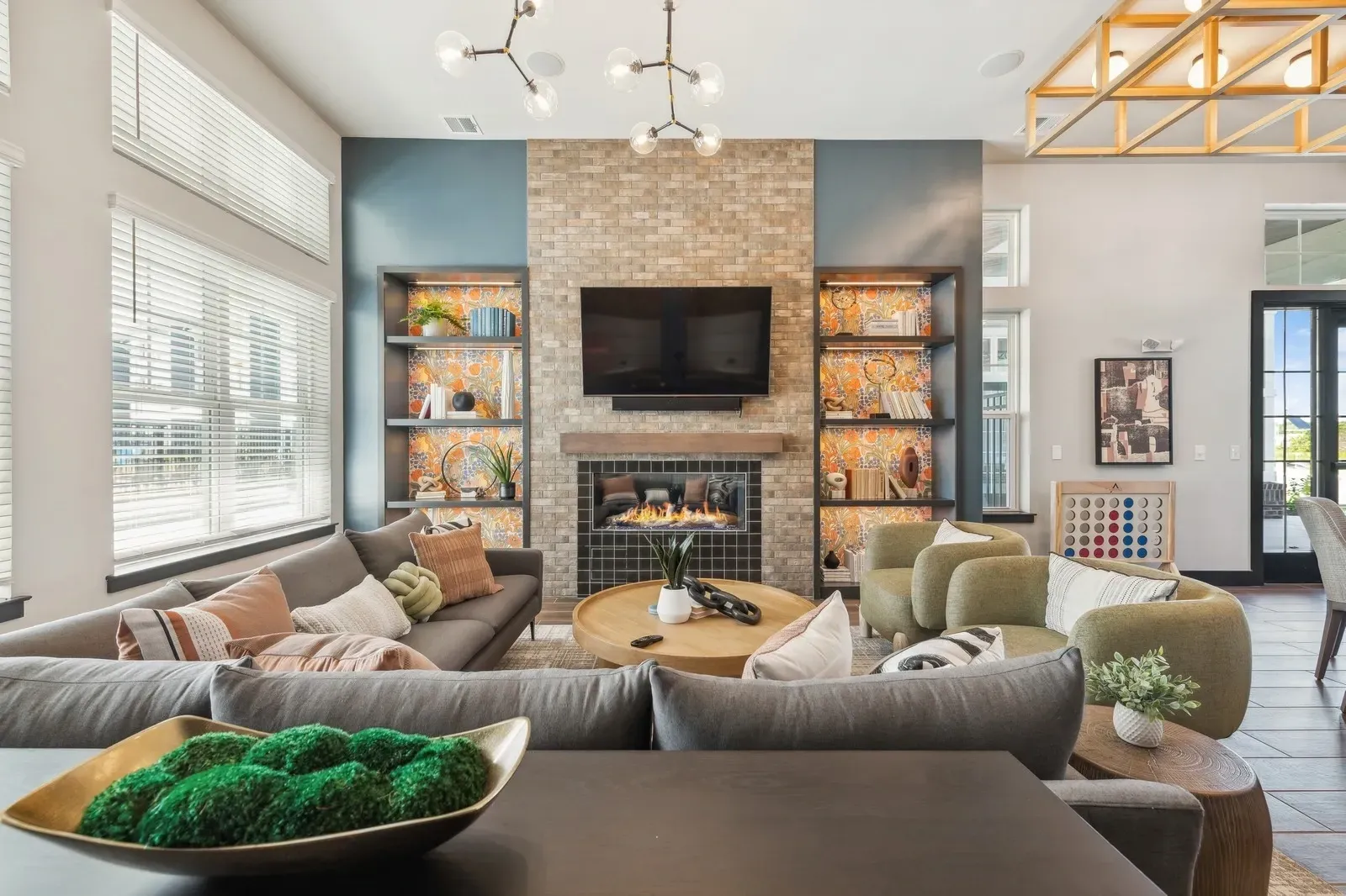 Bright modern community lounge with a brick fireplace, TV, and built-in shelving