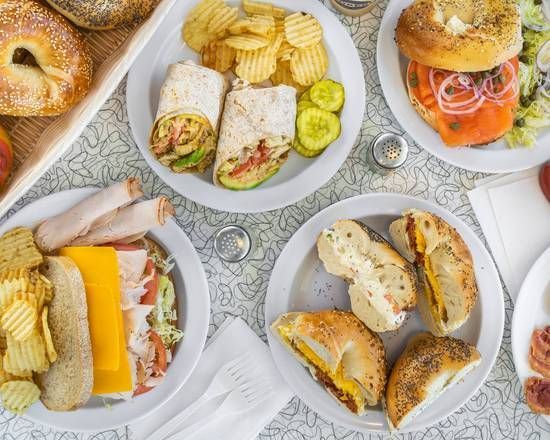 A table topped with plates of food including bagels sandwiches and chips.